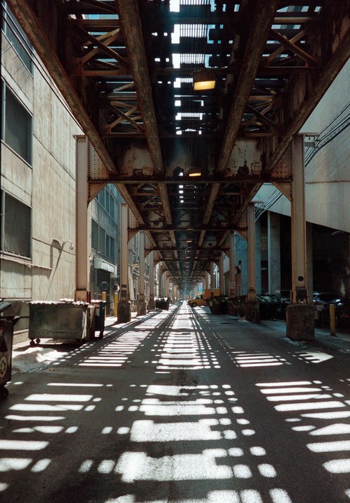 A long alleyway is covered in shadows from an elevated train track in Chicago.