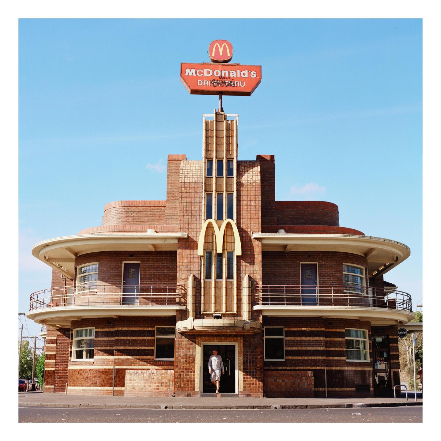 A man exits a McDonald's restaurant with an art deco facade and a large sign on the roof.