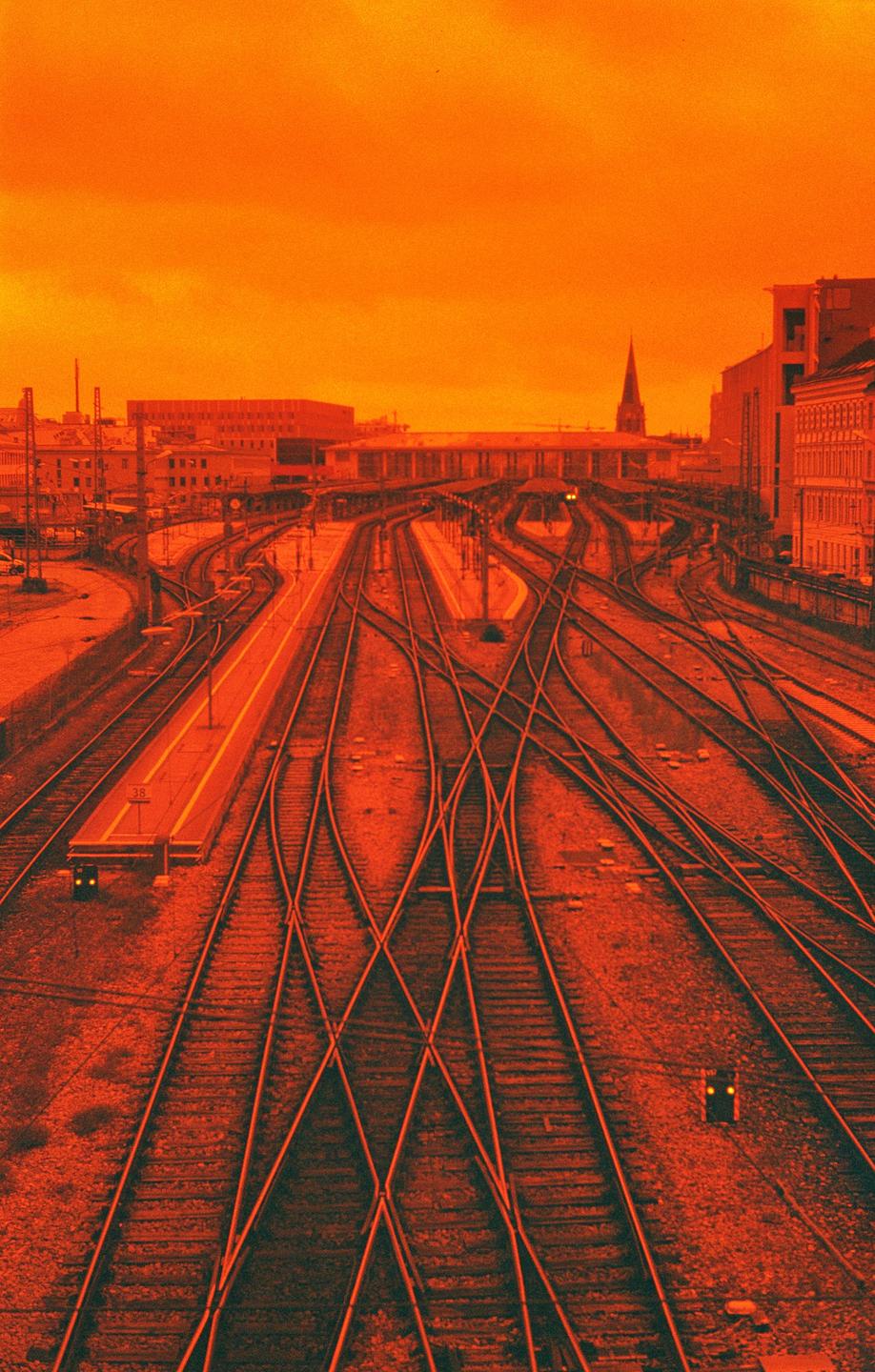A train station with multiple tracks and platforms is visible under an orange sky.