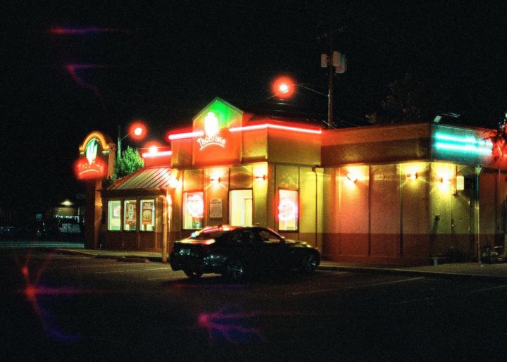 A car is parked in front of a Taco Time restaurant at night.