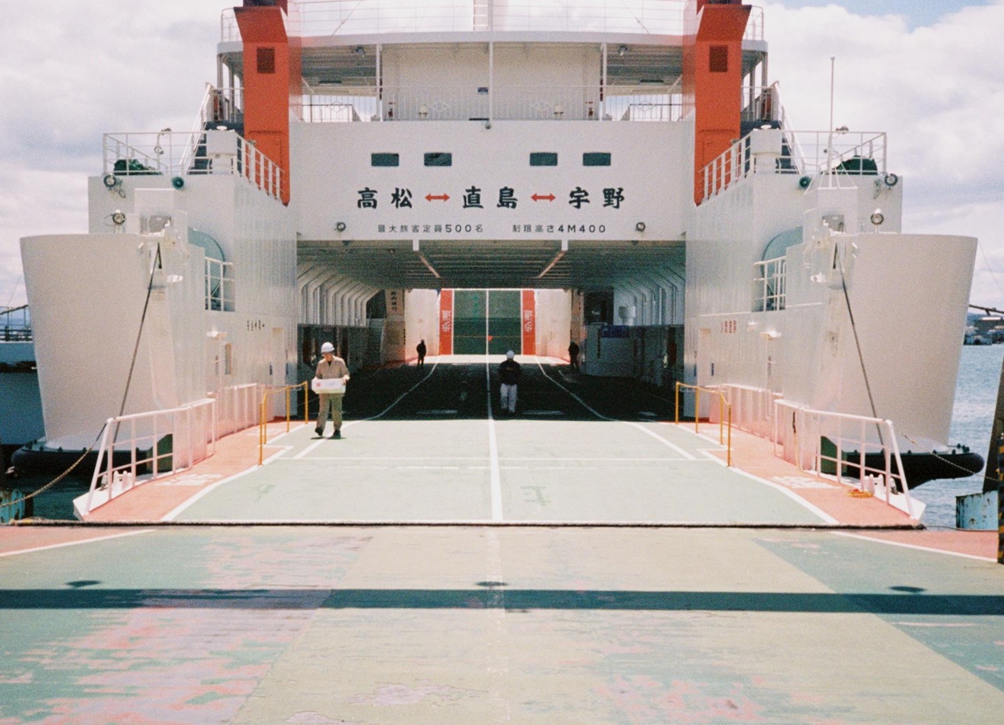 A man walks on the deck of a ferry with Japanese writing on its stern.