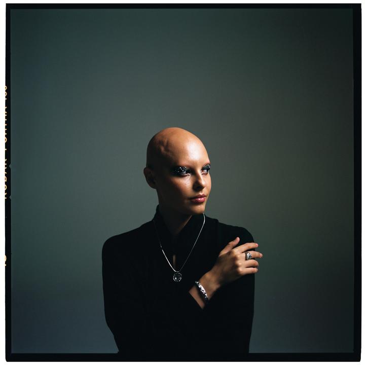 A woman with a bald head and dark clothing looks to the side.
