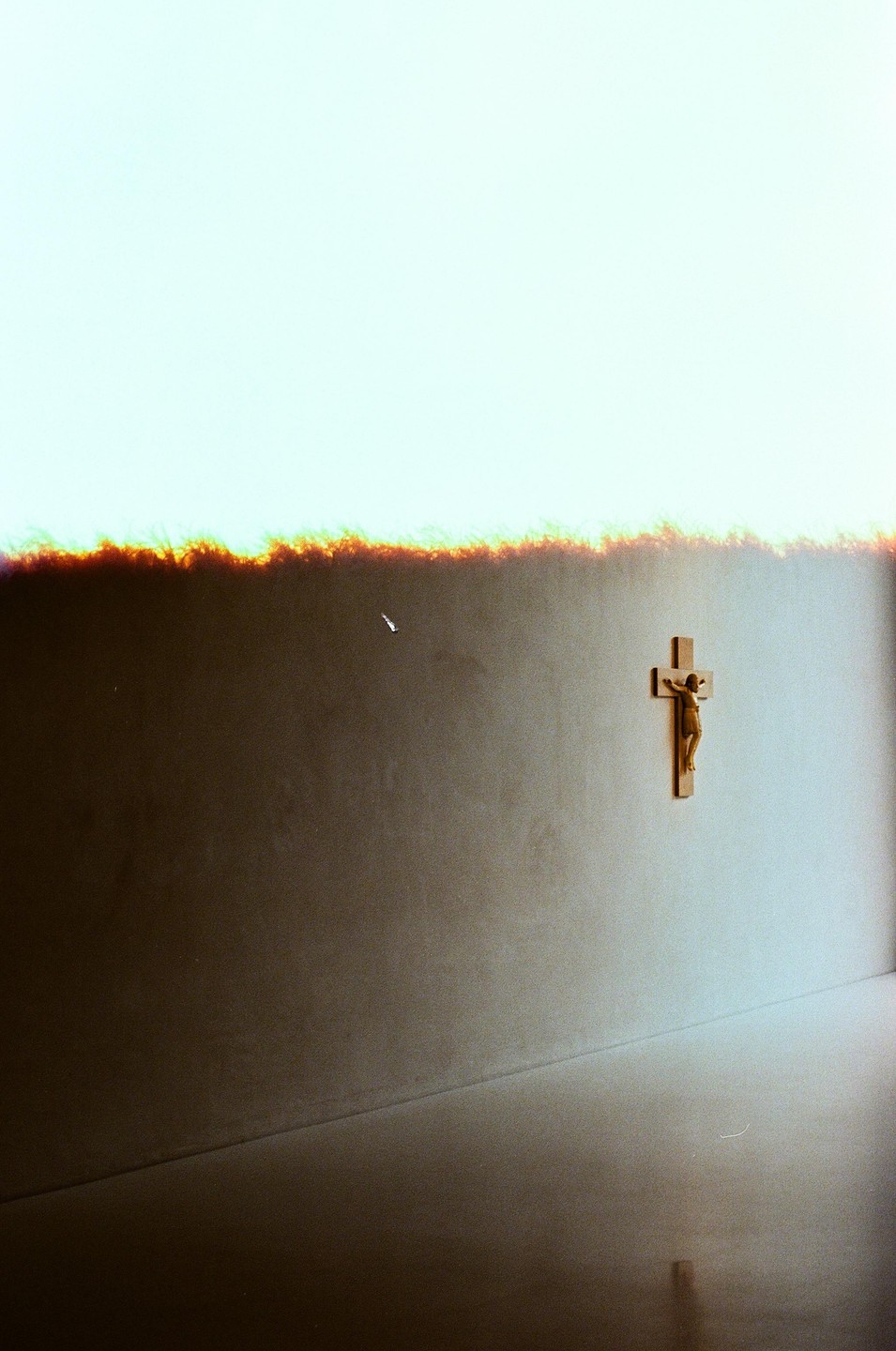A crucifix hangs on a wall with a bright light source above it.