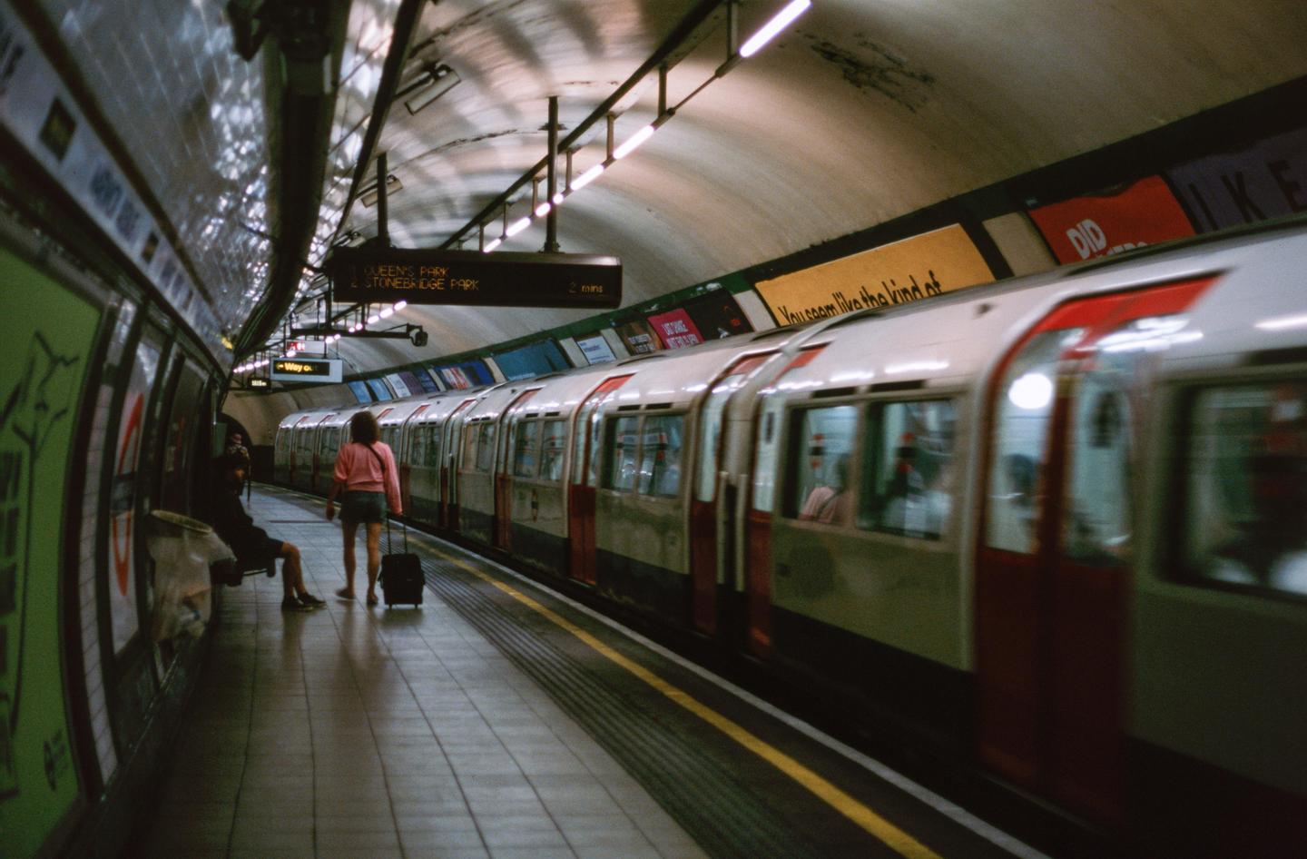 A woman with a suitcase stands on a subway platform as a train pulls into the station.