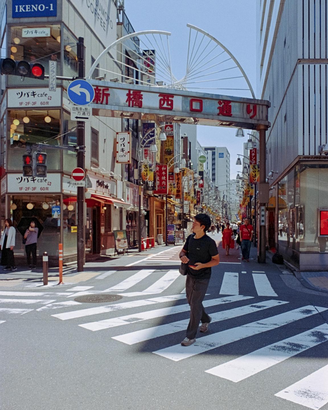 A man crosses a street at an intersection with many buildings and signs.