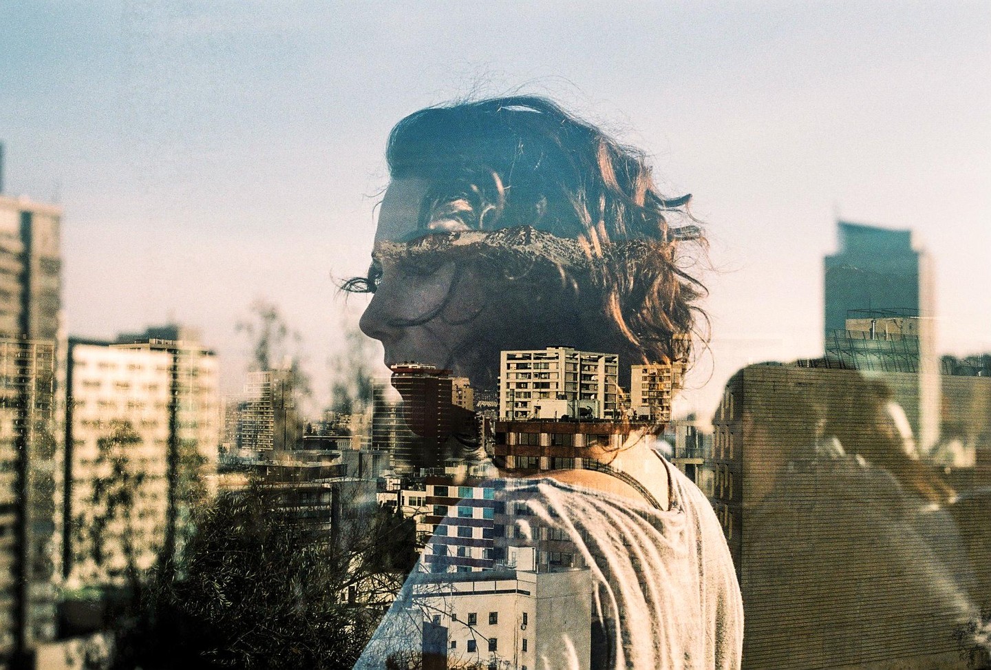 A double exposure shows a woman's profile overlaid with a cityscape under a bright sky.