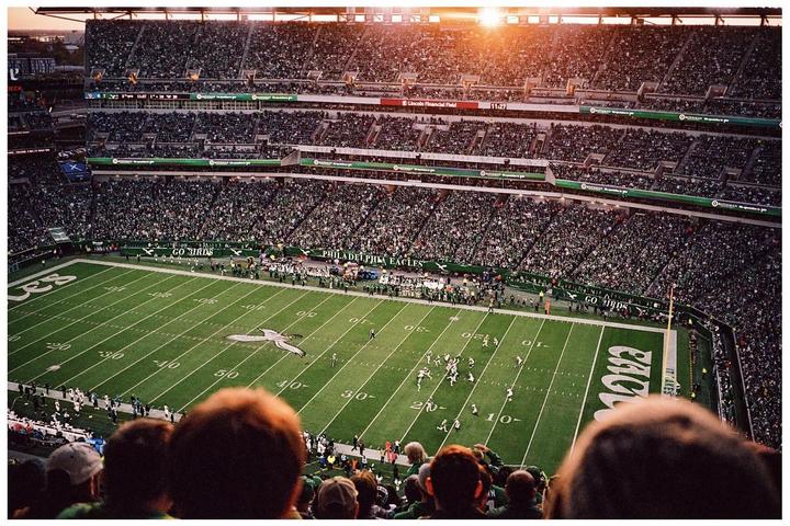 A football game is being played in a stadium filled with spectators during sunset.