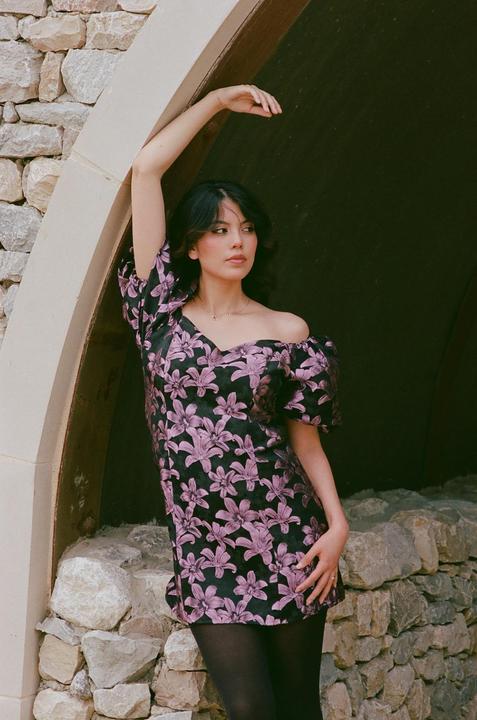 A woman in a floral dress poses in a stone archway.