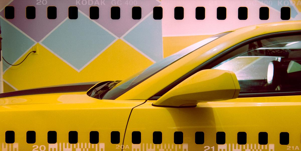 A yellow car is parked in front of a wall with a geometric pattern.