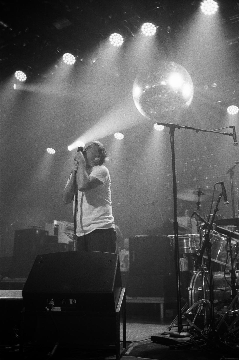 A man sings into a microphone on a stage with a disco ball and stage lights.