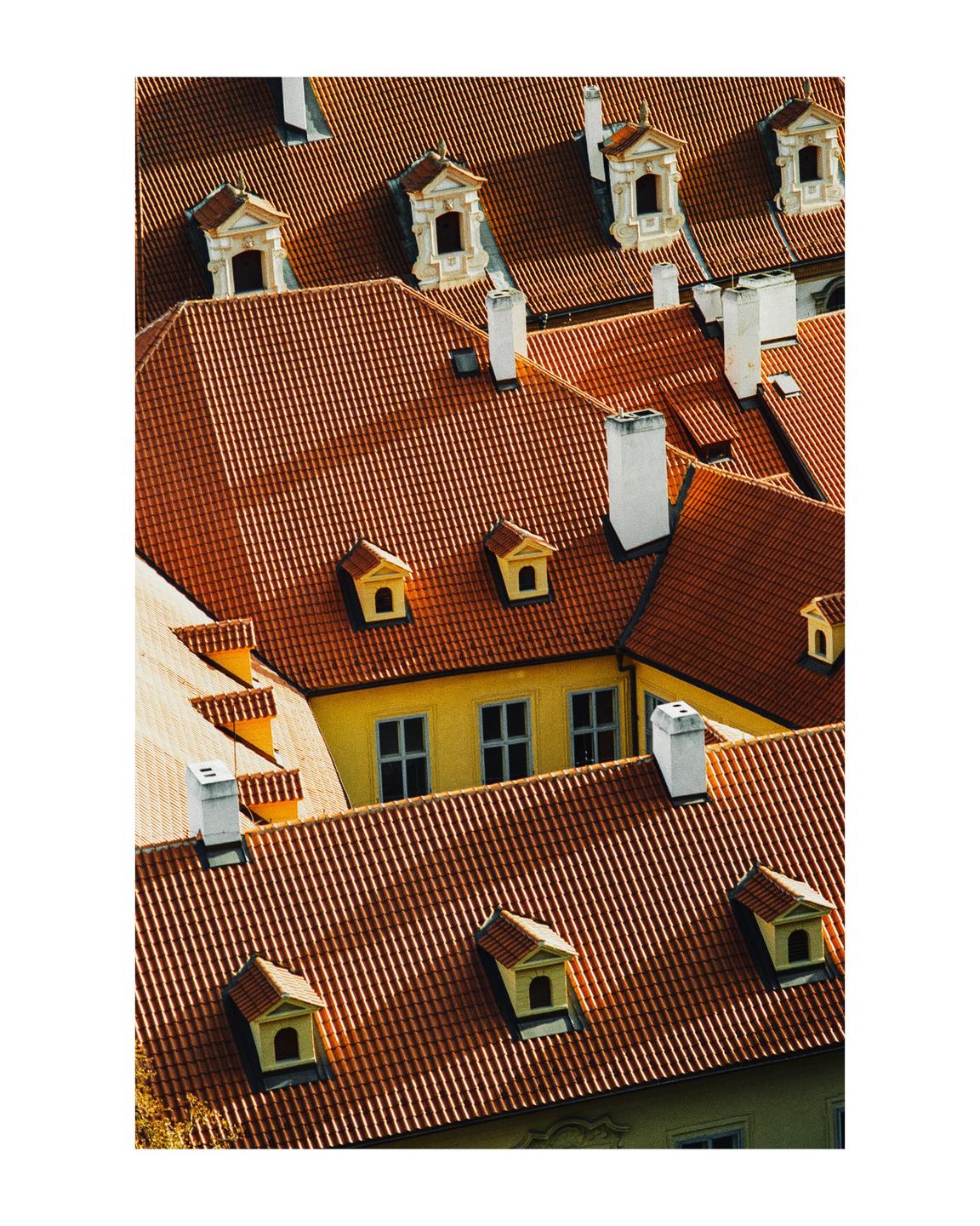 An aerial view shows many red tile rooftops with dormer windows and chimneys.