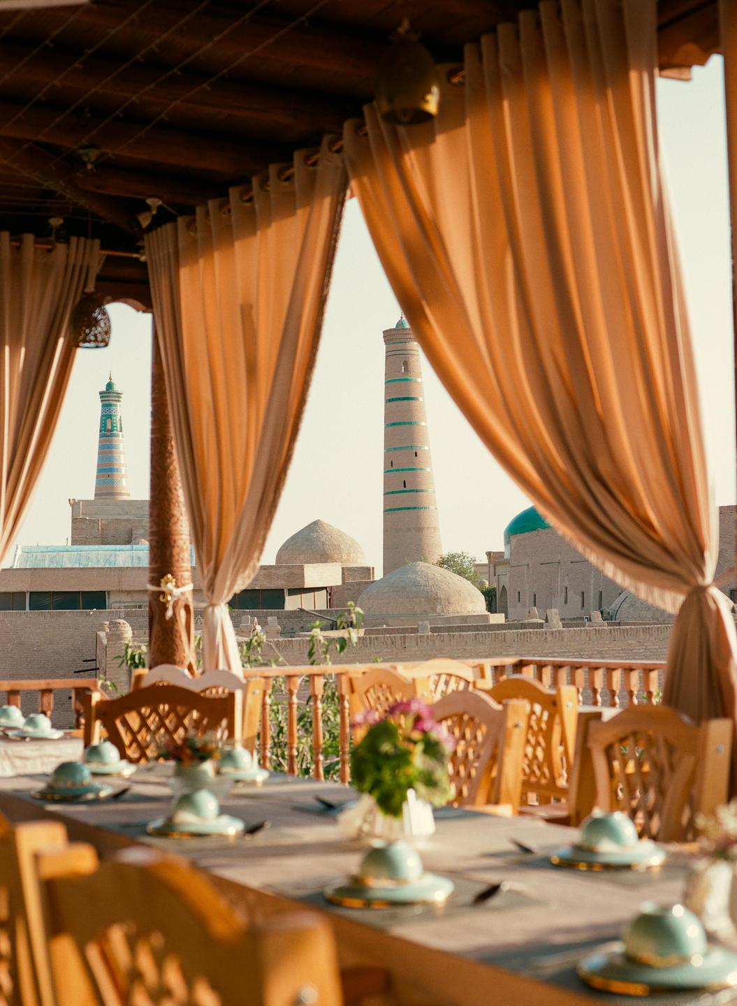 A rooftop restaurant with curtains framing a view of two minarets and domes in a historic city.