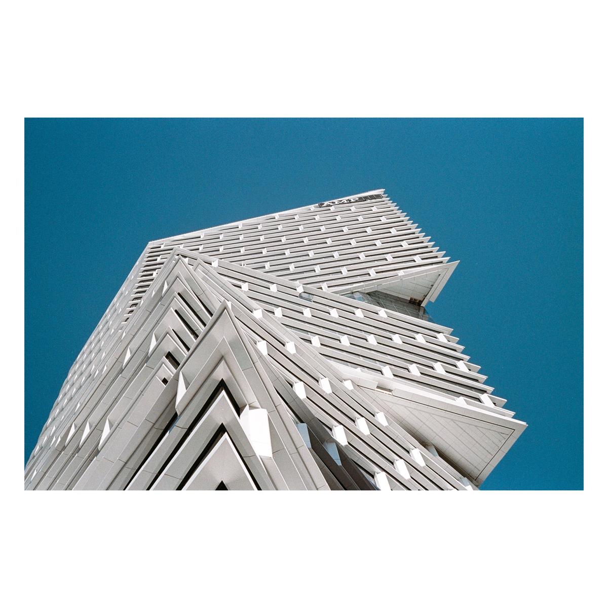 A modern white building with a geometric design stands against a clear blue sky.