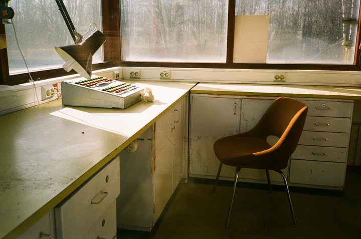 A desk lamp illuminates a control panel with colorful buttons next to a window overlooking a forest.