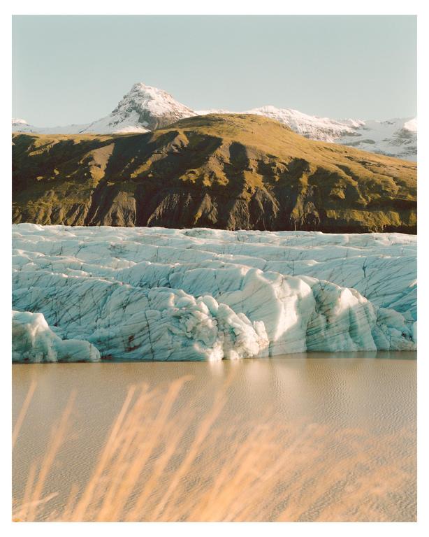 A glacier meets a body of water with a mountain in the background under a clear sky.