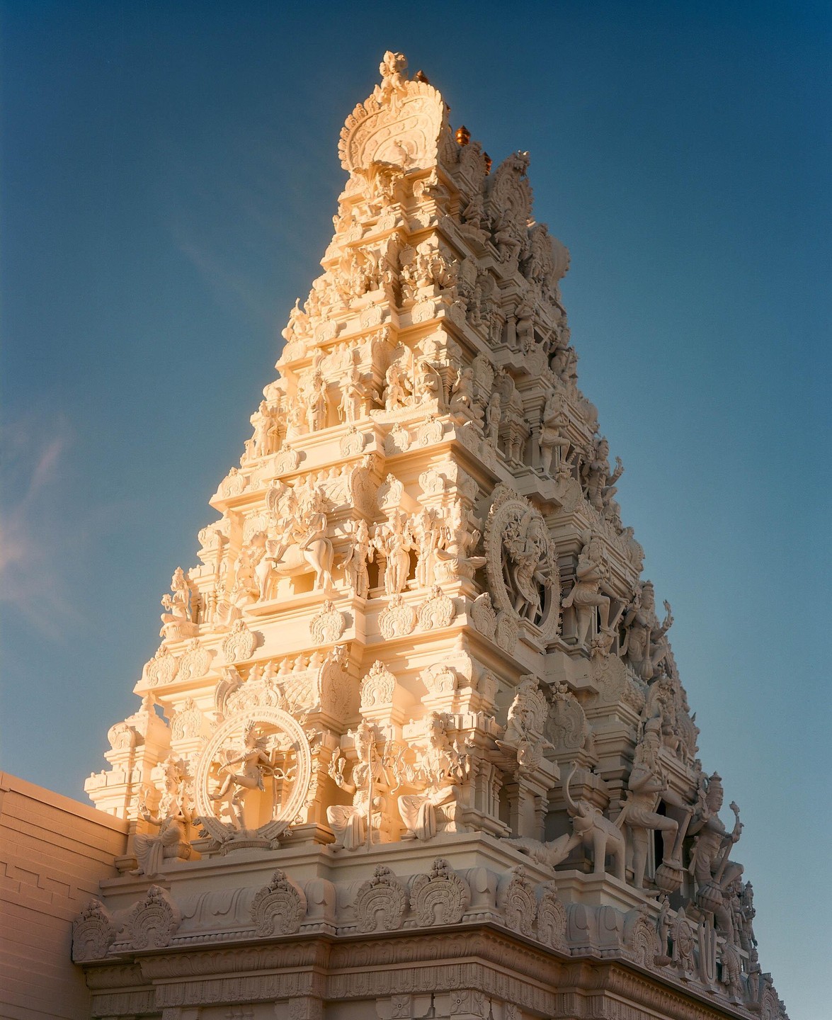 A tall, intricately carved white temple tower stands against a clear blue sky.