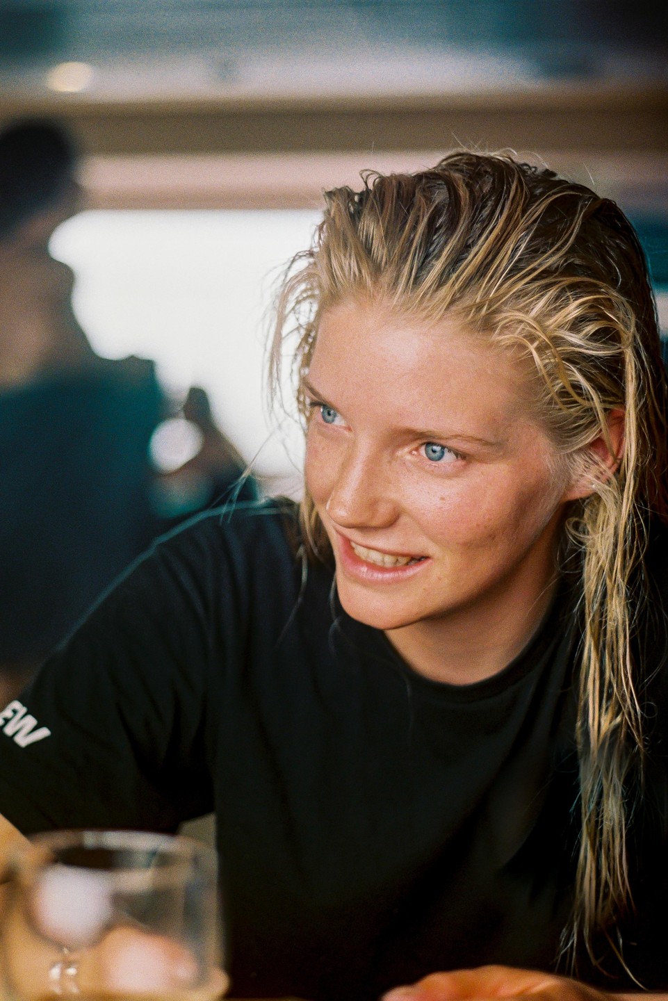 A woman with wet blonde hair and blue eyes smiles while looking to the right.
