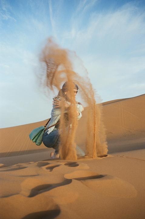 A person kneels in a desert, with sand falling from their hands.