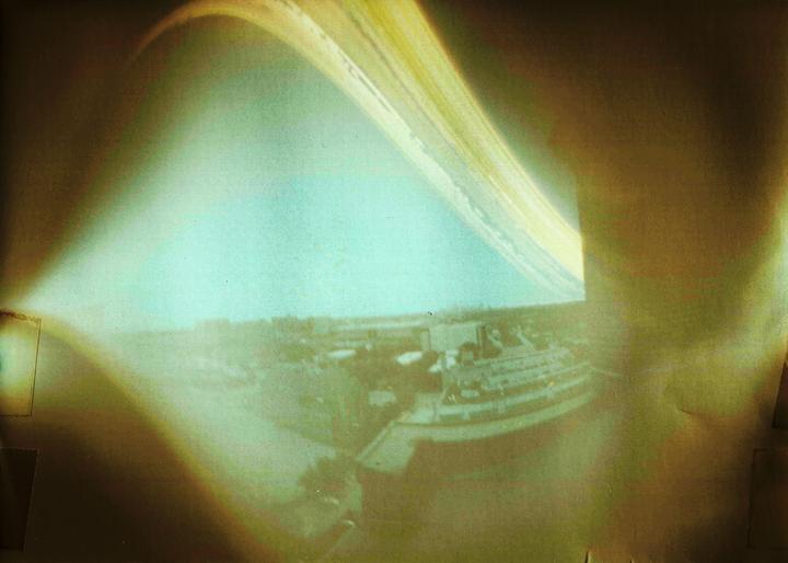 A long exposure photograph shows a bright arc across a hazy sky above a cityscape.