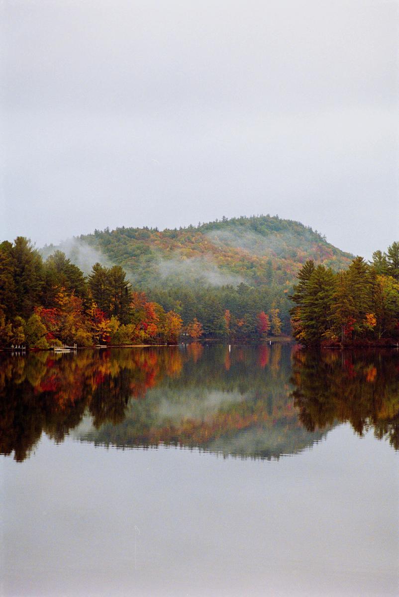 A lake reflects a forest with autumn foliage and a hazy mountain.