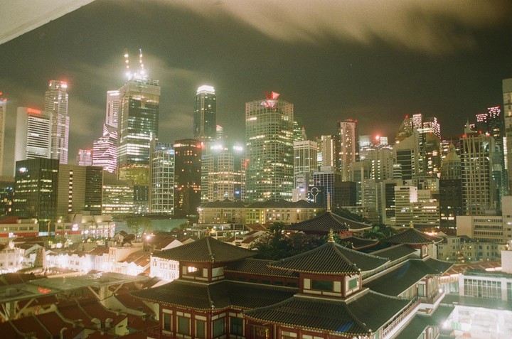 A city skyline at night shows modern skyscrapers behind traditional buildings with ornate roofs.