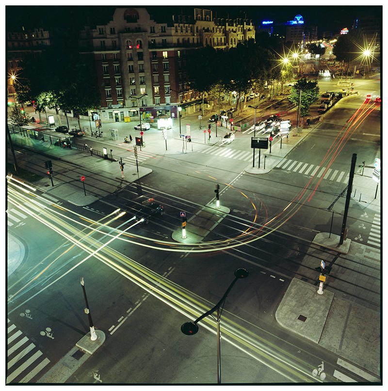An elevated view shows a city intersection at night with light trails from vehicles.