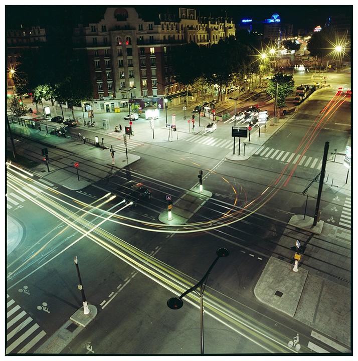 An elevated view shows a city intersection at night with light trails from vehicles.