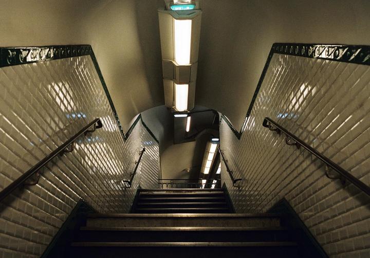 A long staircase with white tiled walls and handrails descends into a subway station.