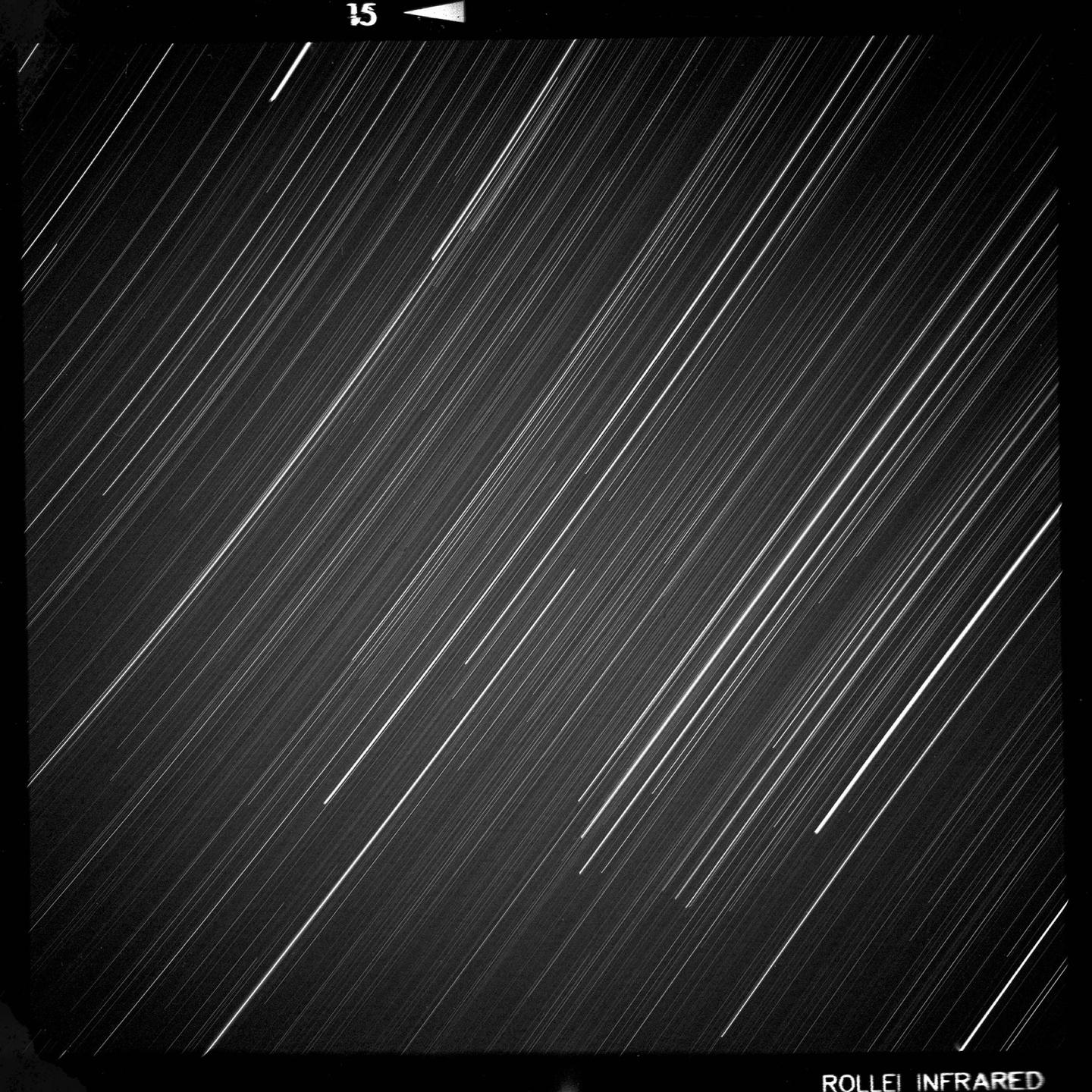 Numerous bright star trails streak across a dark night sky.