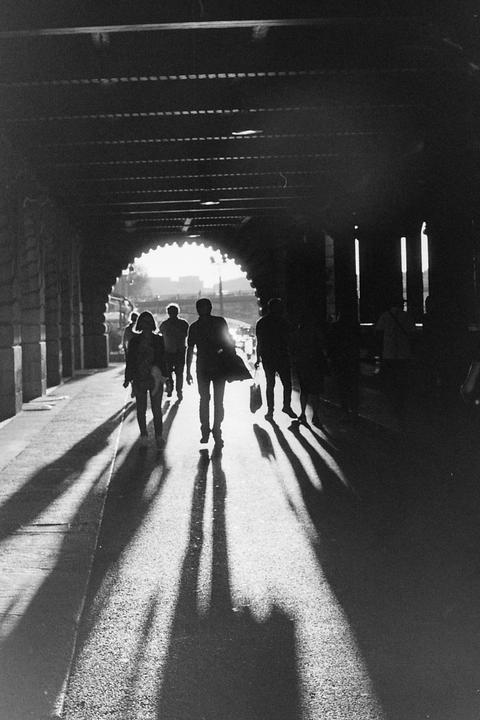 People walk through a dark tunnel with bright light at the end, casting long shadows on the ground.