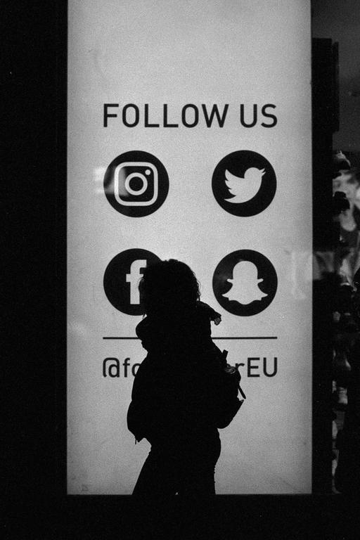 A person is silhouetted against a sign with social media logos and the text "FOLLOW US".