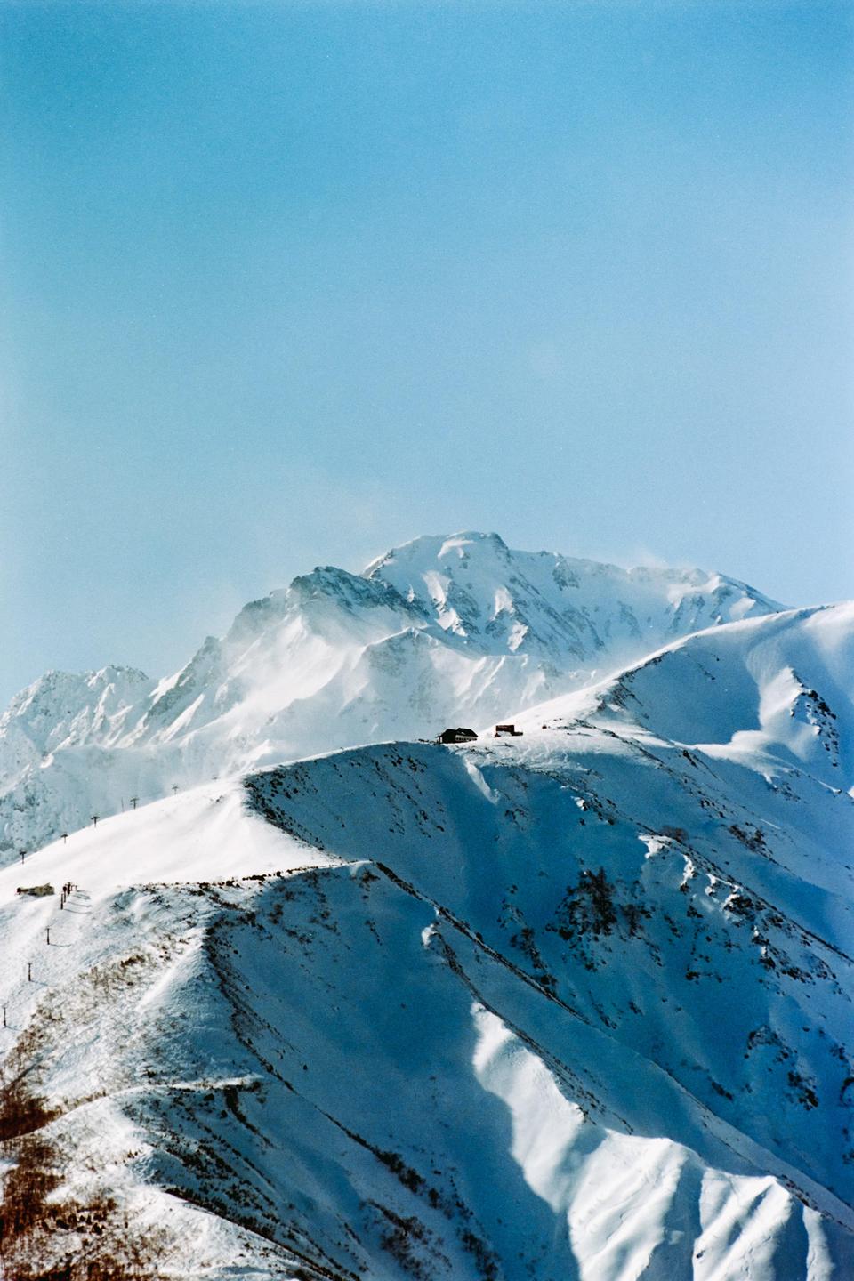 A snow-covered mountain range with a few buildings on a ridge is visible under a clear sky.