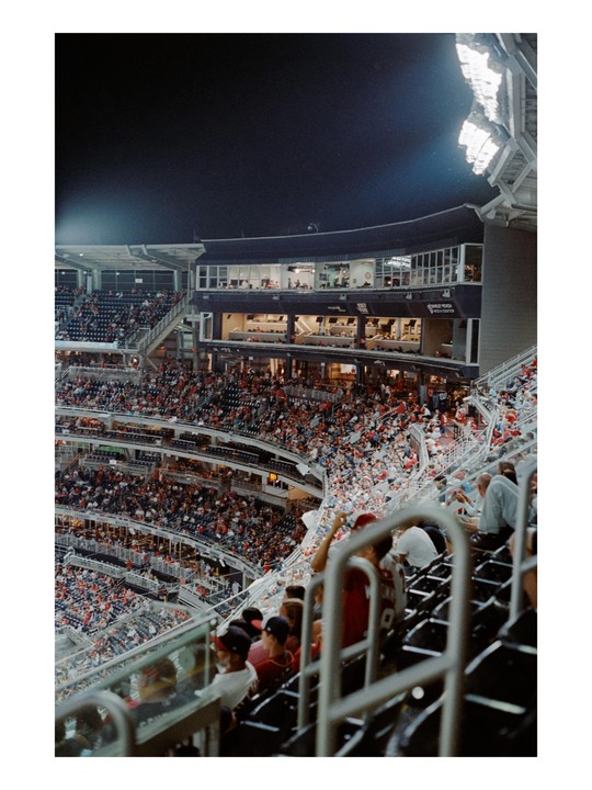 A stadium is filled with spectators at night, with bright lights illuminating the field.