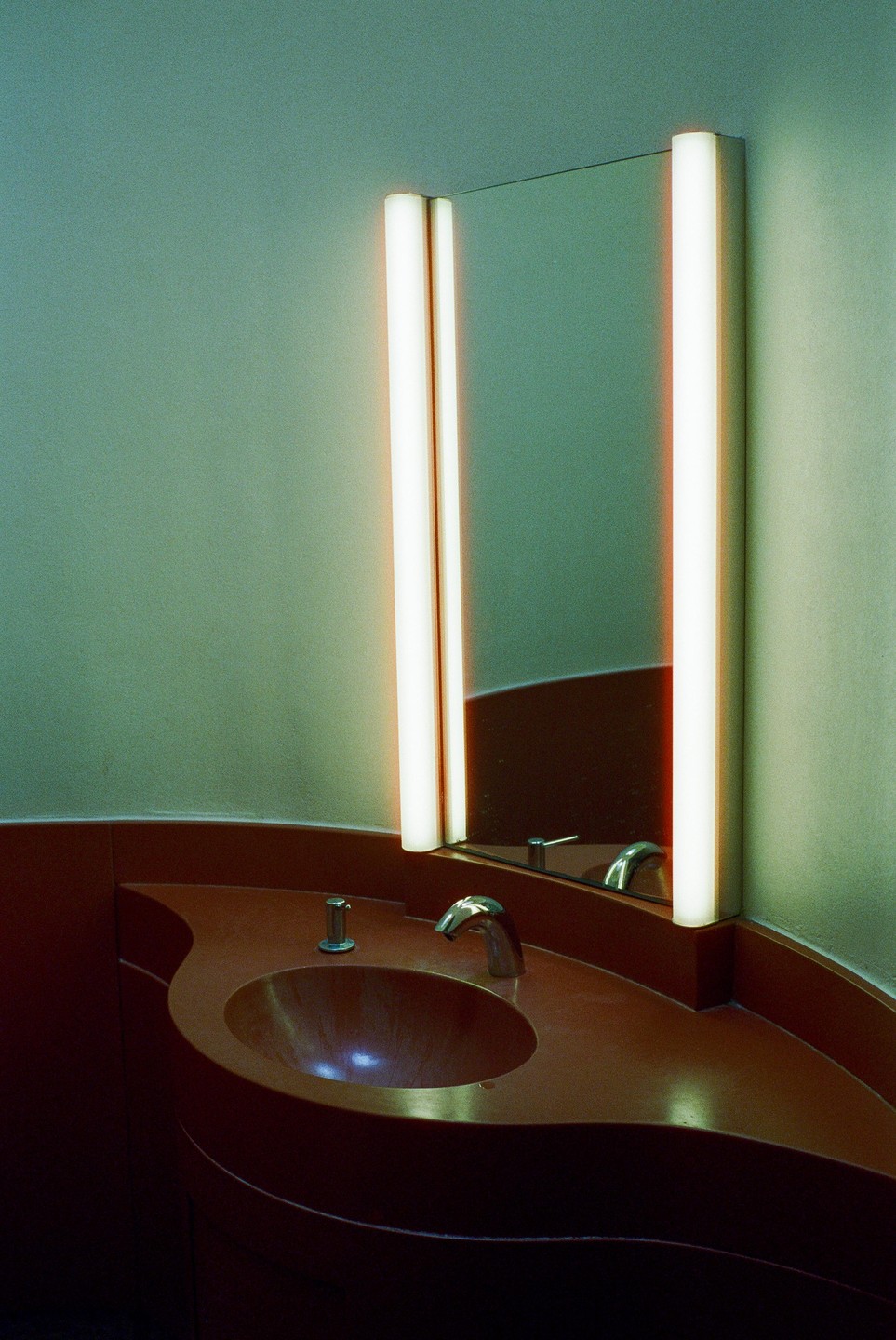 A red sink with a faucet and soap dispenser is visible below a mirror flanked by two vertical lights.