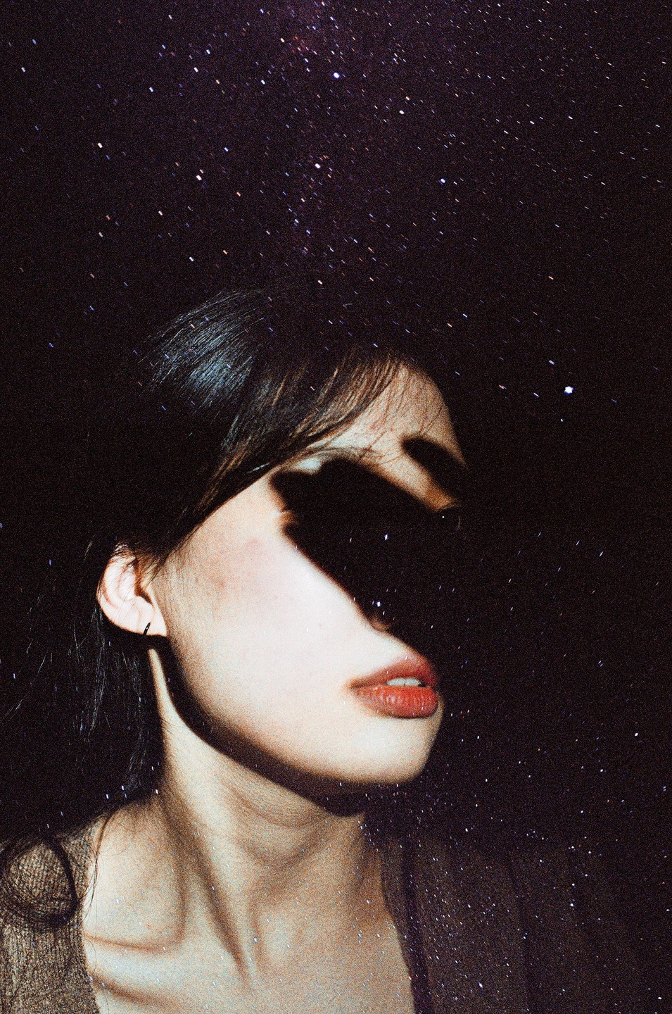 A woman's face is partially obscured by shadow against a starry night sky.