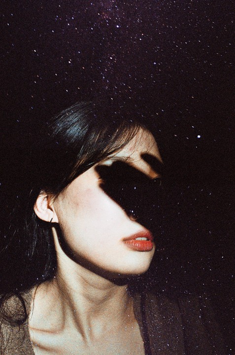 A woman's face is partially obscured by shadow against a starry night sky.