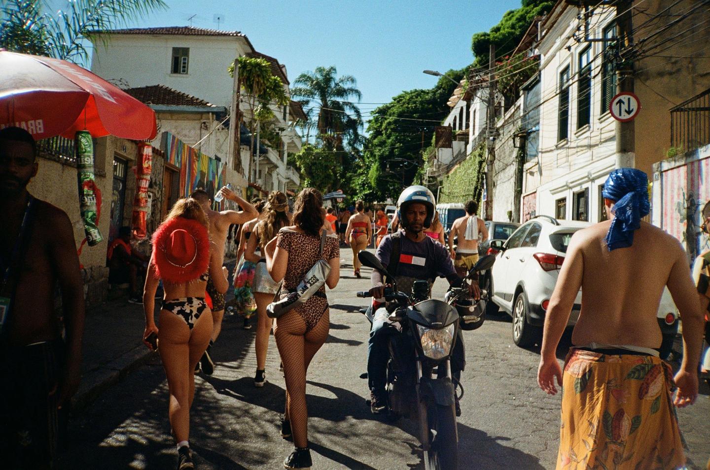 A street is filled with people, some in costumes, and a man on a motorcycle.