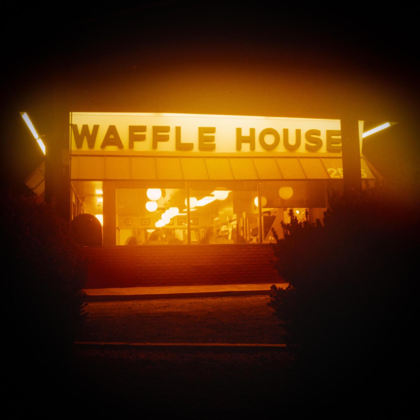 A Waffle House restaurant is brightly lit at night, with dark bushes in the foreground.