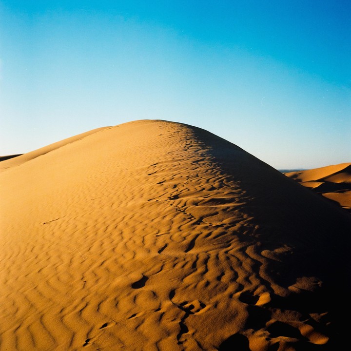 A large sand dune with ripples and shadows is visible under a clear blue sky.