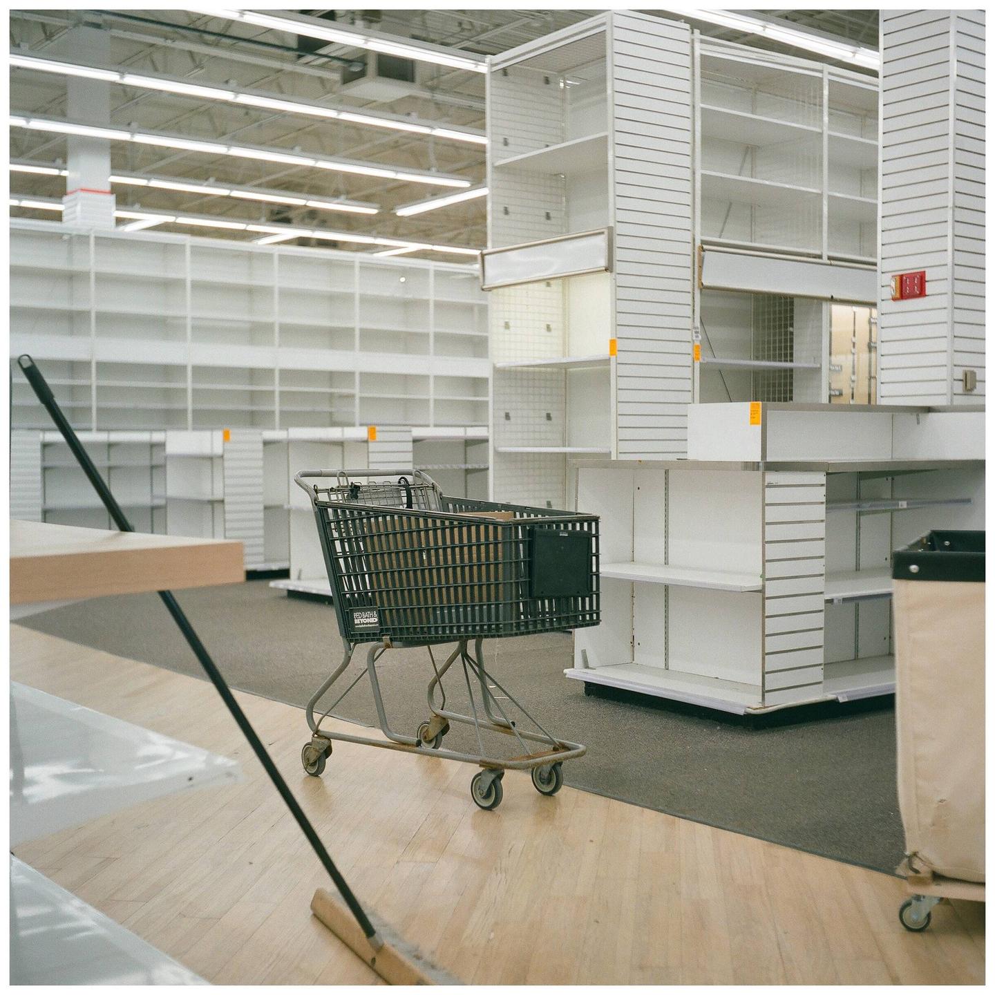 A shopping cart sits in an empty store with white shelves.