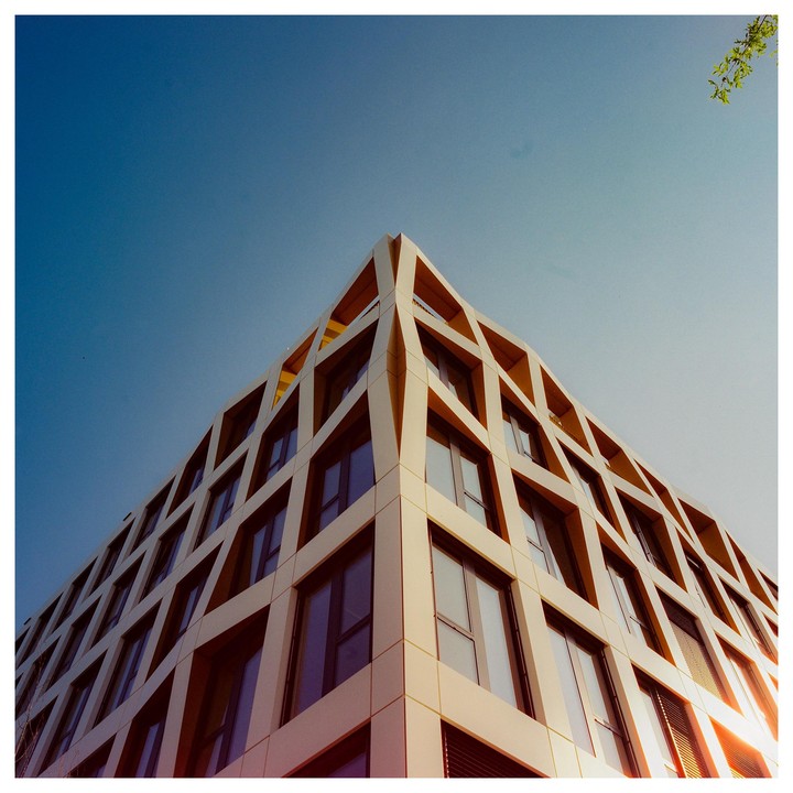 A modern building with a geometric facade is viewed from below against a clear sky.