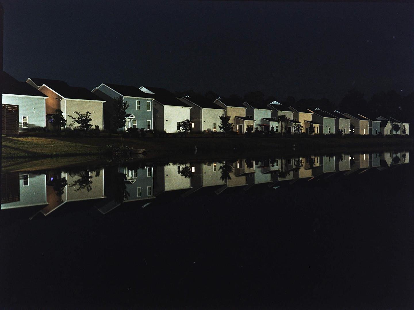 A row of houses with illuminated windows is reflected in a body of water at night.