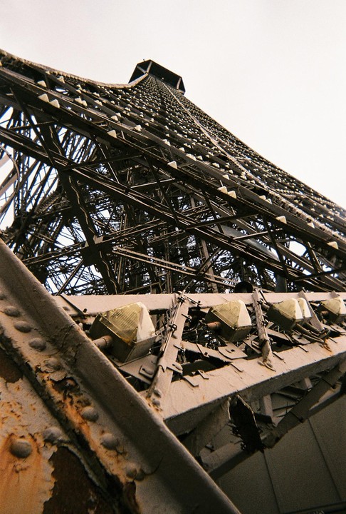The Eiffel Tower is viewed from below, showing its intricate metal structure and lights against a bright sky.
