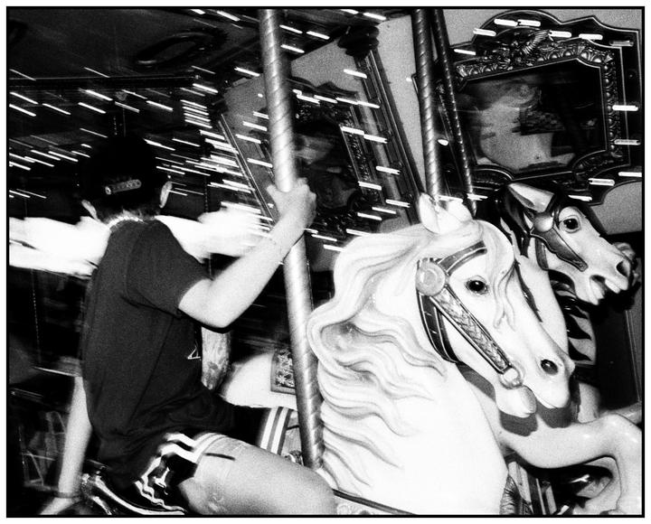 A person rides a carousel horse, with motion blur visible in the background.