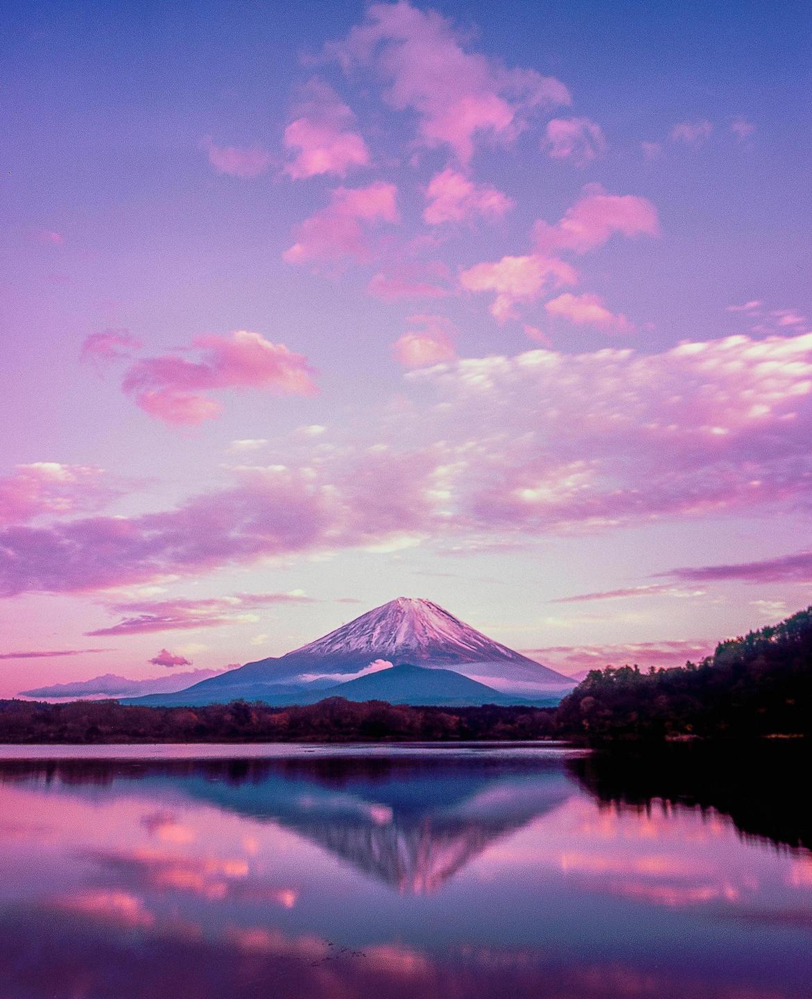 A snow-capped mountain is reflected in a lake under a sky with pink clouds.