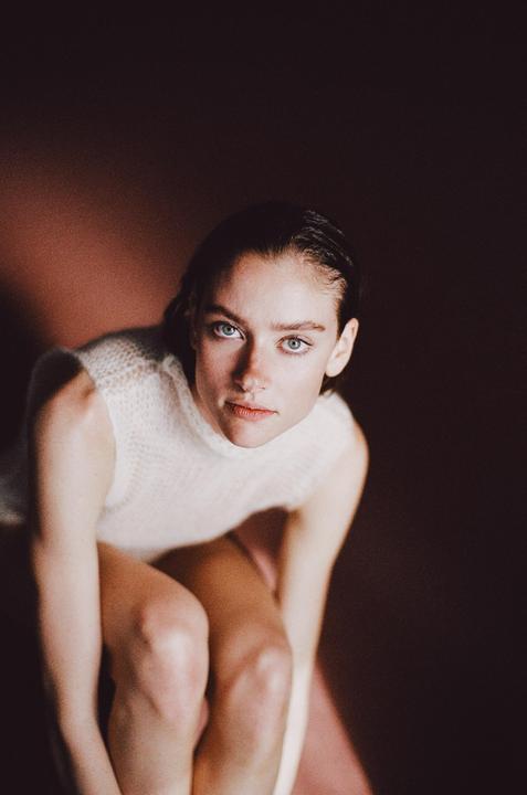 A woman with wet hair and a white top looks up at the viewer.