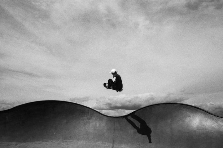 A skateboarder is captured mid-air above a skate park ramp, with their shadow cast on the ramp below.