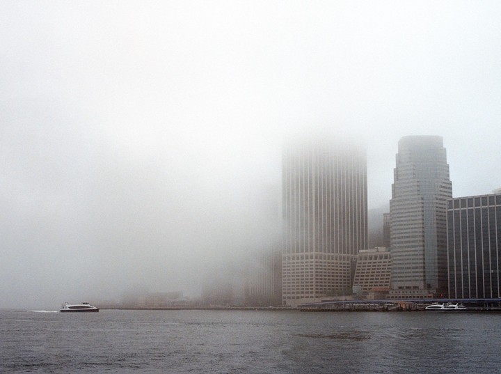 A ferry boat moves across a body of water with a foggy city skyline in the background.