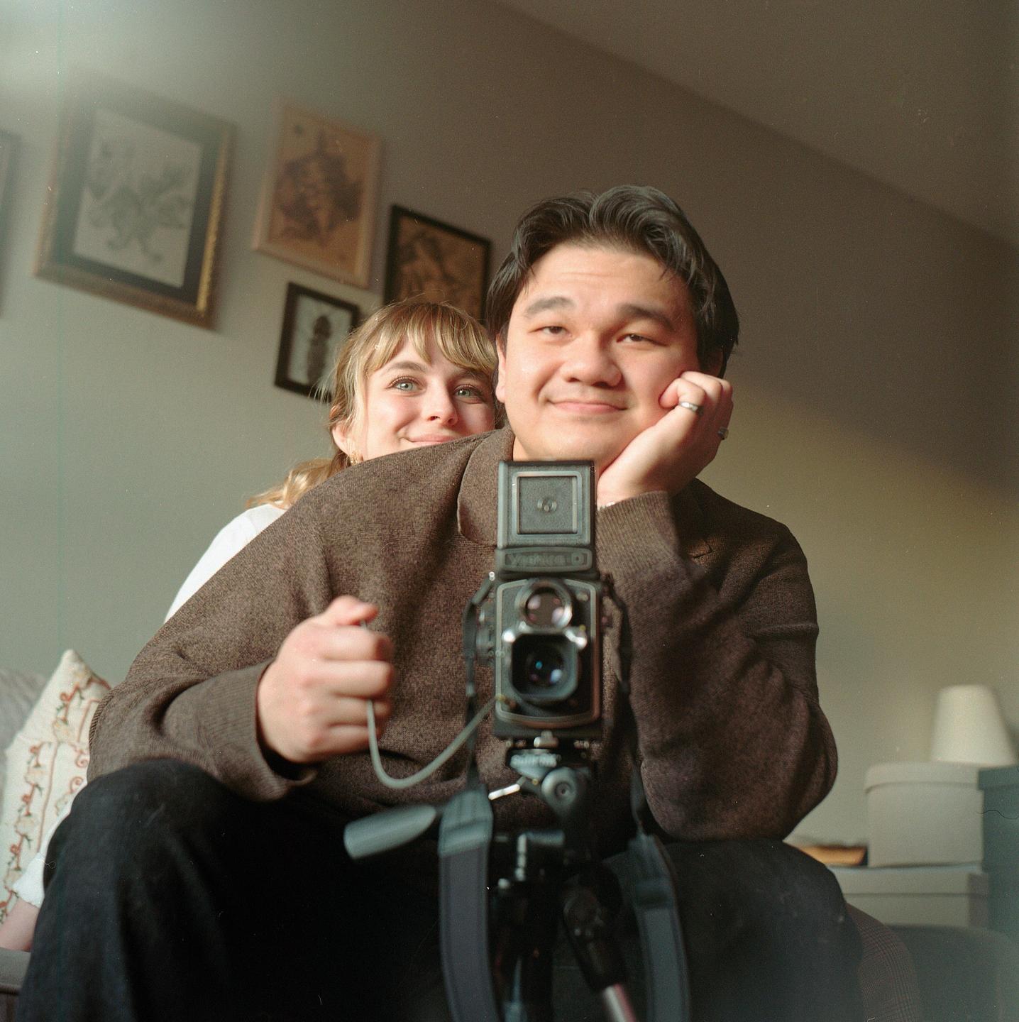 A man and a woman are sitting in a room, looking at the camera.