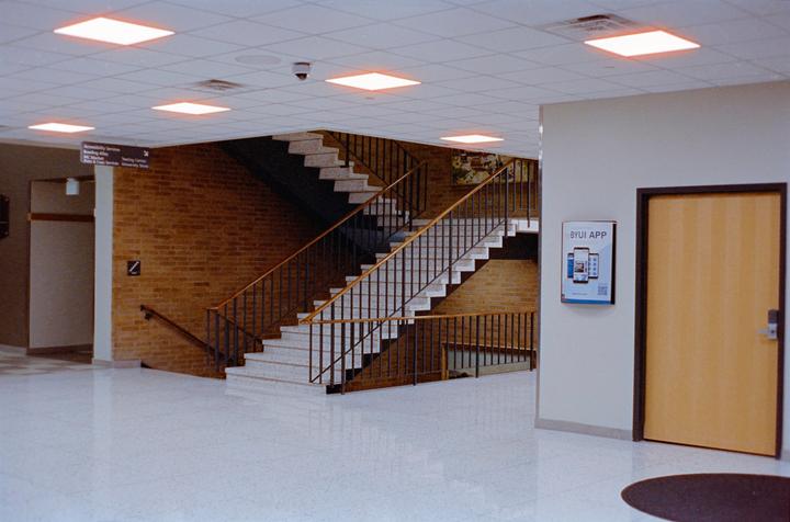 A wide shot shows a staircase with a brick wall and a door with a sign on the right.